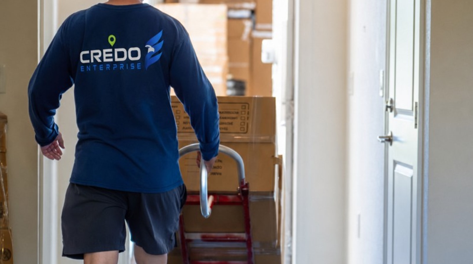 Credo Enterprise mover wheeling stacked boxes on a dolly through a condo hallway
