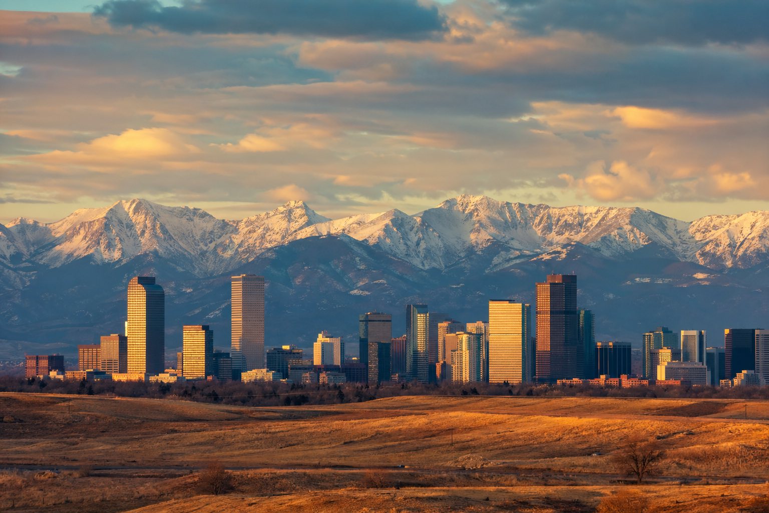 Modern photograph of the Denver skyline with the Rocky Mountains backdrop at golden hour representing Credo Enterprise' Colorado service area