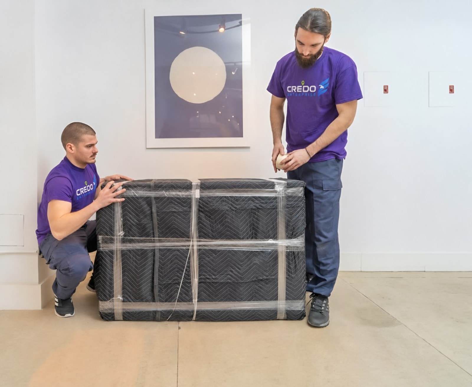 Credo Enterprise packers in branded uniforms wrapping furniture with heavy-duty moving blankets and professional shrink wrap indoors